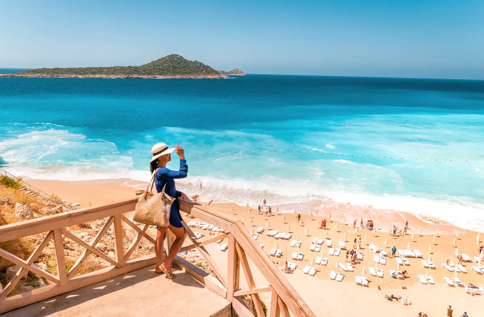 Junge Frau mit Hut im blauen Kleid auf Anhöhe blickt an einem schönen Sommertag auf den Strand von Kaputas herab.